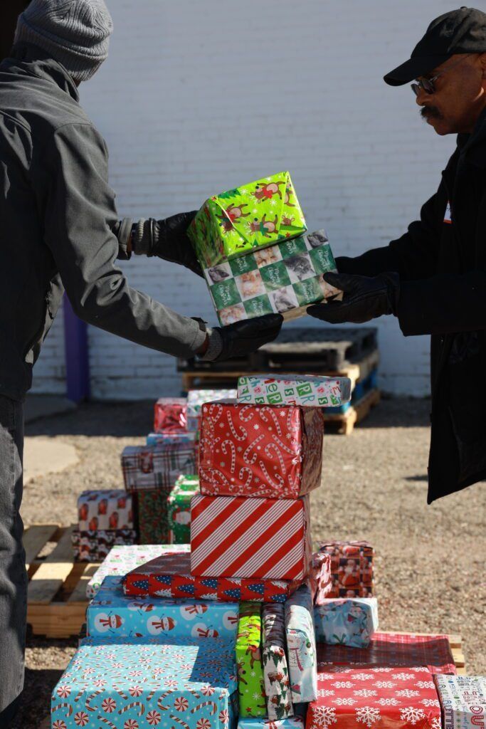 People stacking colorful wrapped gift boxes outdoors, with two others passing a green present.
