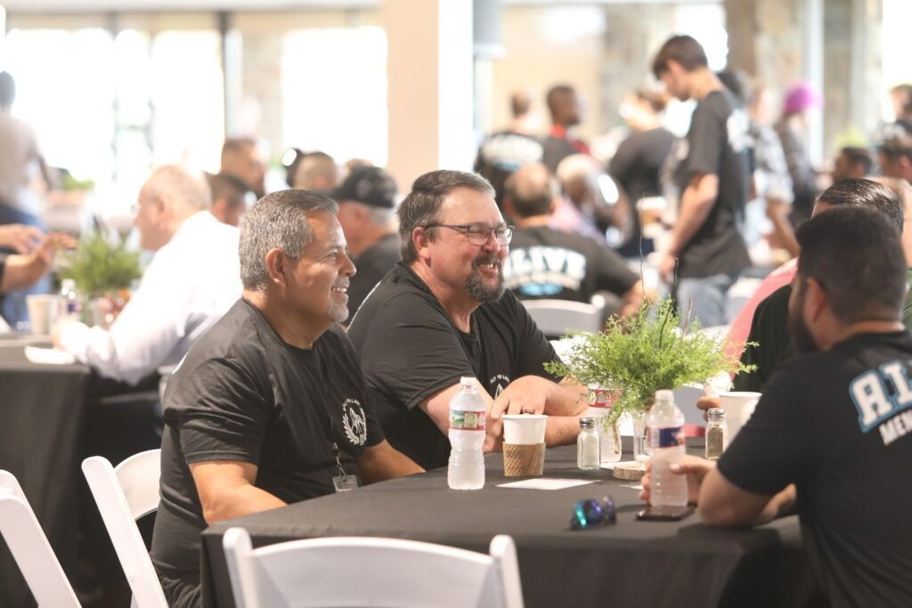 People seated at tables in a bright indoor dining area, chatting and eating at a social event