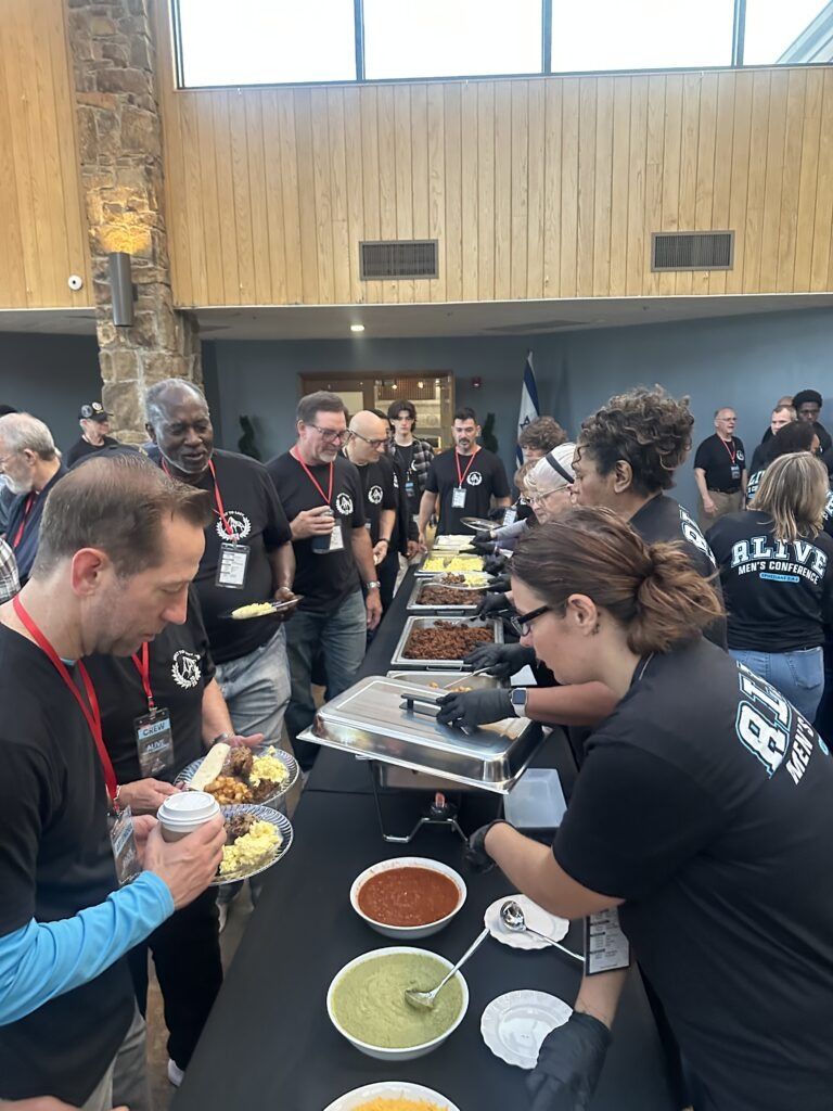People serving and receiving food at a buffet line in a busy indoor event hall
