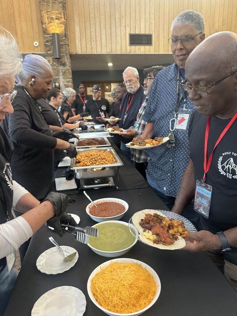 People serving themselves from a buffet table with trays of food in a banquet hall