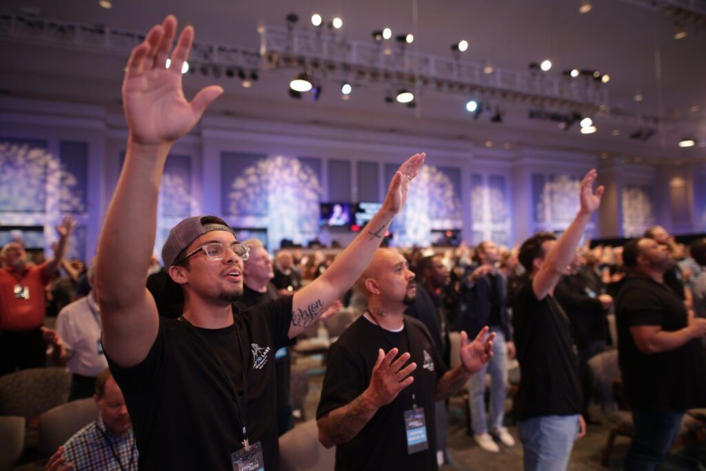 People standing with hands raised at a conference or worship gathering in a large hall