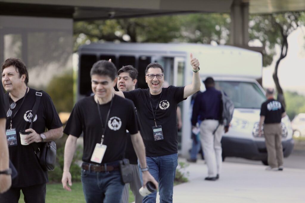 Several people in black T-shirts walking outside a building near a van