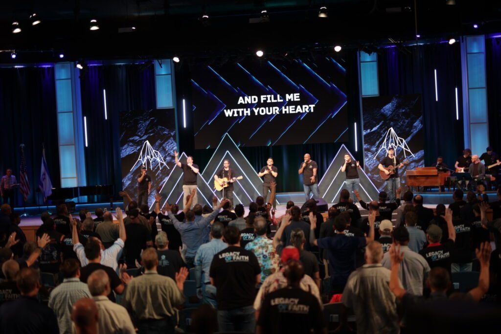 Crowd at a concert worship service with a lit stage and screen reading “I will fill you with my…”
