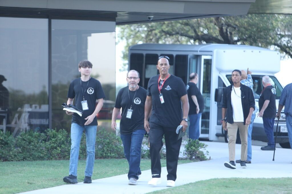 People walking outside a modern building, with glass windows and a parked vehicle in the background