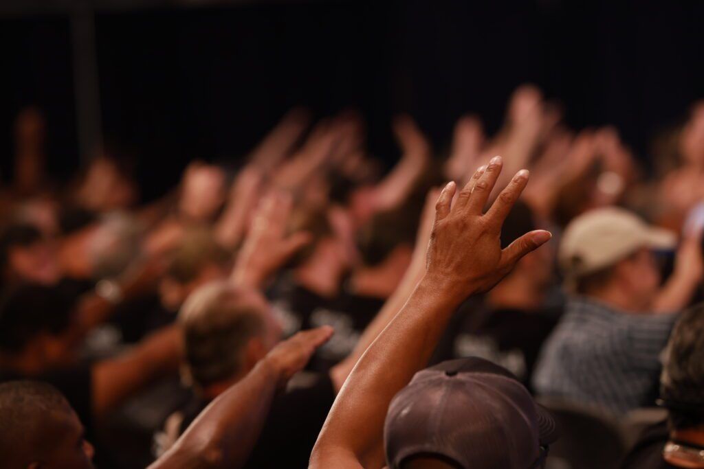 Audience with raised hands at a live event, blurred crowd in the background