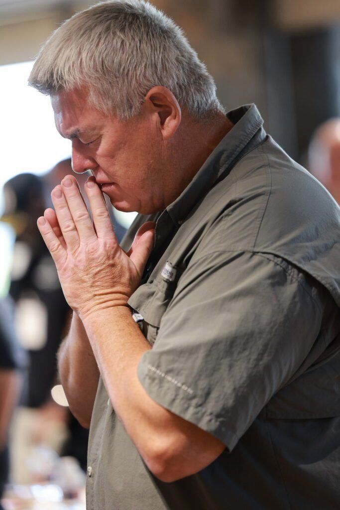 Person with hands clasped in prayer, head bowed in a quiet indoor setting.