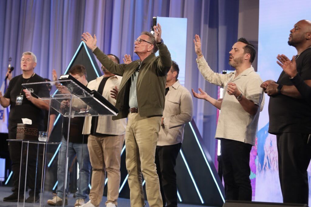People on a stage raising their arms beside a clear lectern and glowing triangular lights