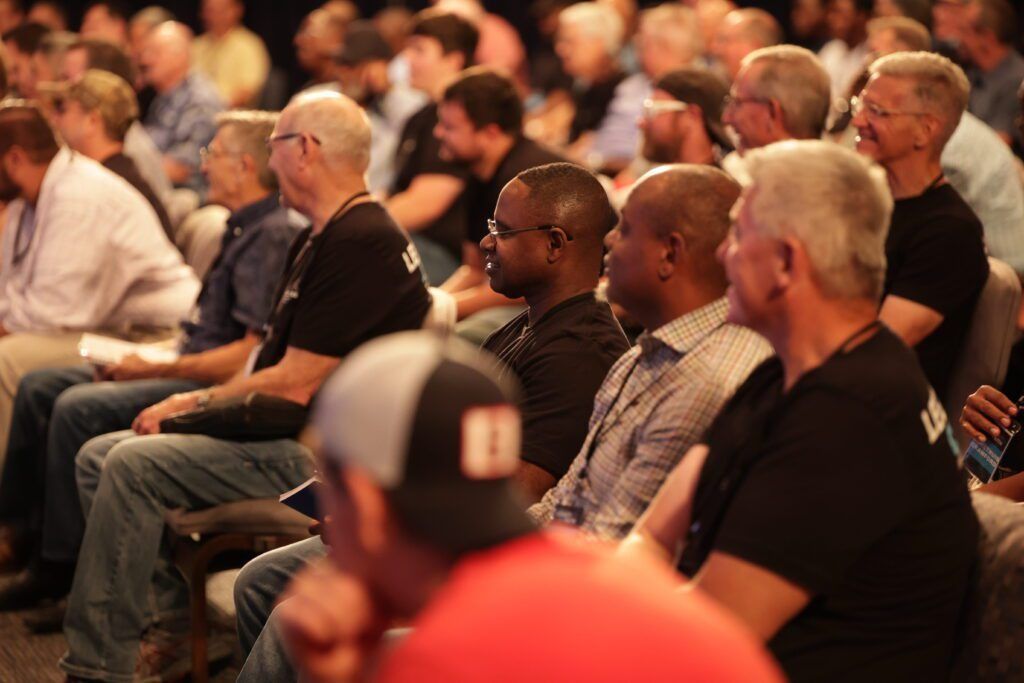 Audience seated in a warmly lit auditorium, listening attentively