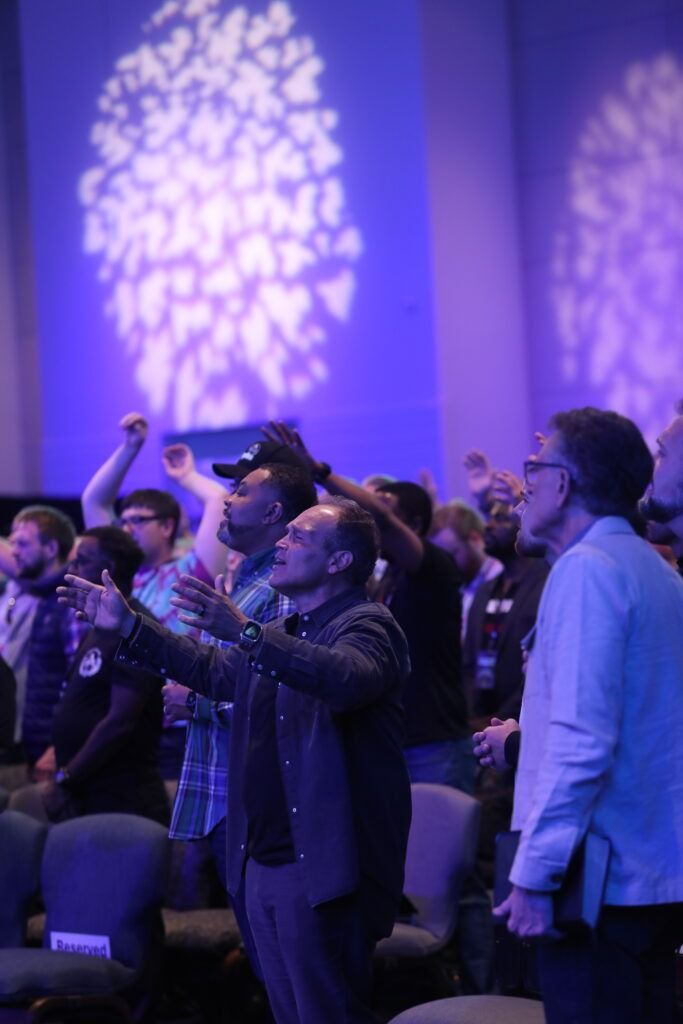 Audience standing and cheering under purple stage lights at an indoor event