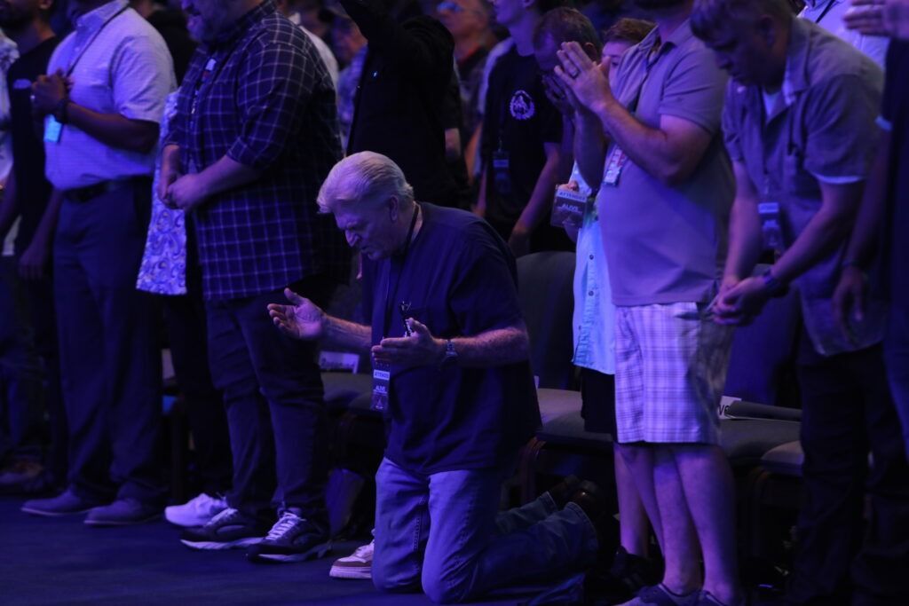 People standing and clapping at a dimly lit event with blue-purple lighting