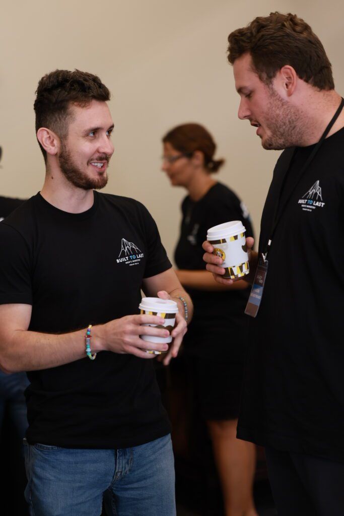 Two people in black shirts chatting and holding coffee cups indoors