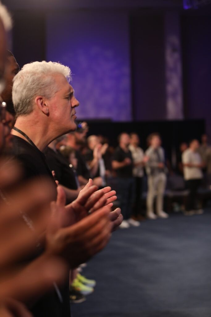 People clapping in a dimly lit conference room with purple lighting and a stage in the background