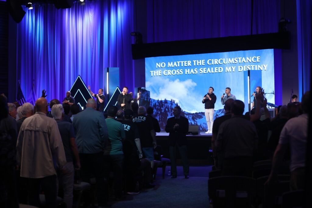 Crowd standing in a blue-lit church auditorium during a worship service on stage.