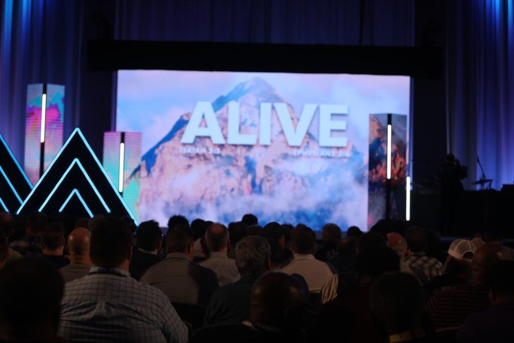 Audience watching a large “ALIVE” stage screen in a dark auditorium