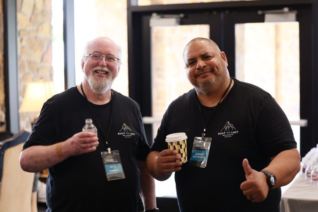 Two smiling men in black shirts holding drinks at an indoor event