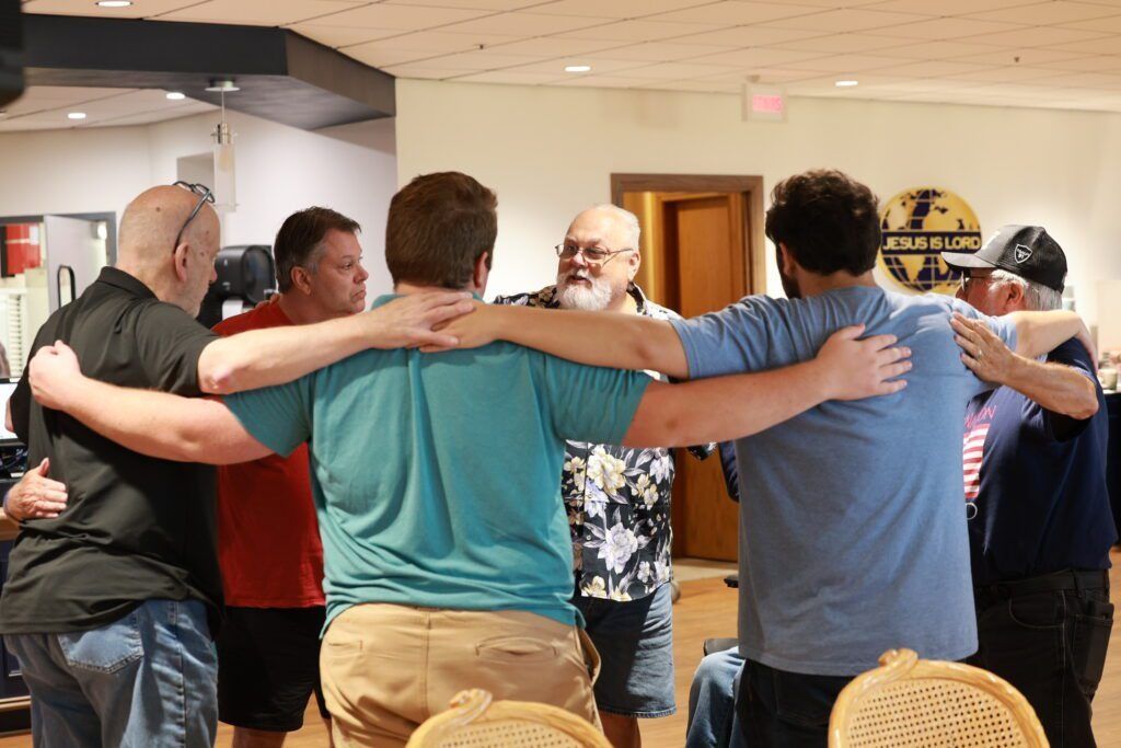 Group of people standing arm-in-arm in a room, facing away from the camera.