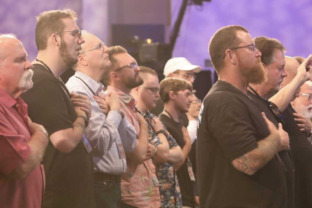 Audience standing and singing at a concert, with hands raised in warm stage lighting