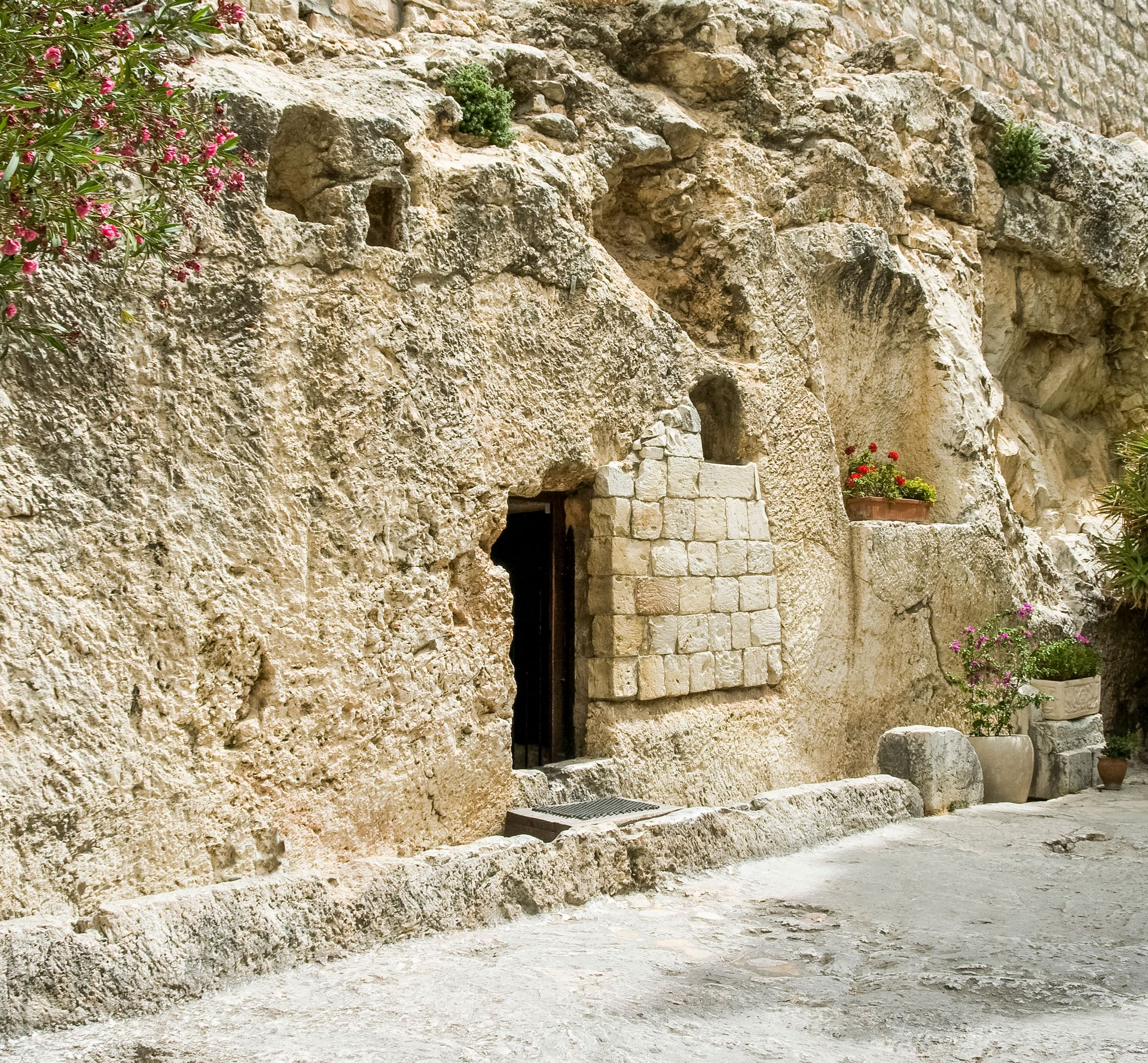 Stone cave dwelling with a wooden door and small windows beside a narrow street, with flowers overhead