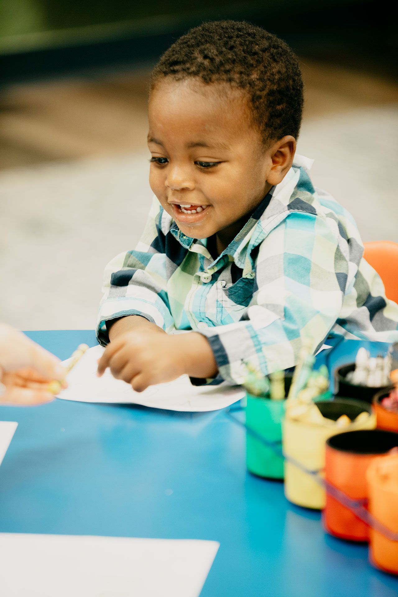 Child smiling while painting at a blue table with colorful art supplies.