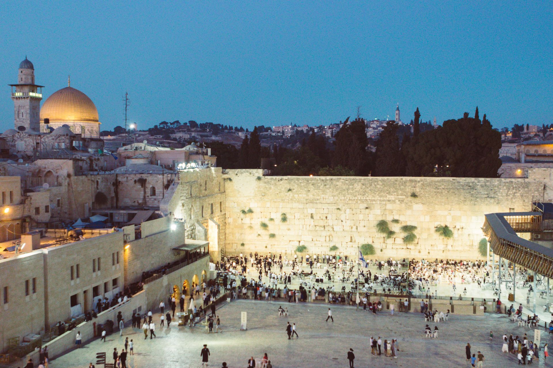Western Wall at dusk with crowds praying, and Jerusalem’s golden Dome of the Rock in the background