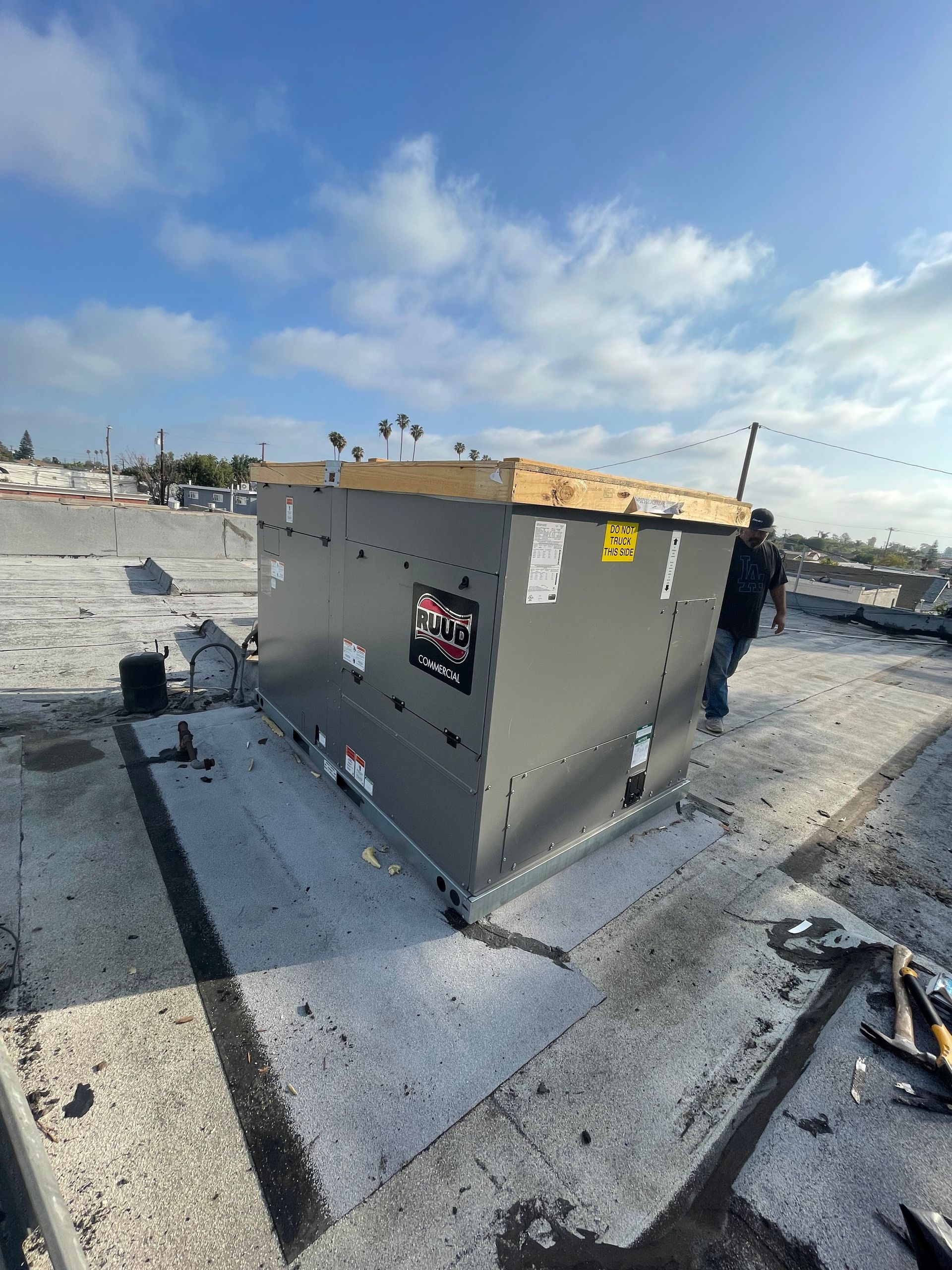 A rooftop air conditioning unit on a flat roof with a person standing nearby on a cloudy day.