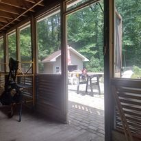 A screened in porch with chairs and a table and a view of the woods.