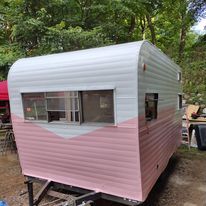 A pink and white trailer is parked in the woods.