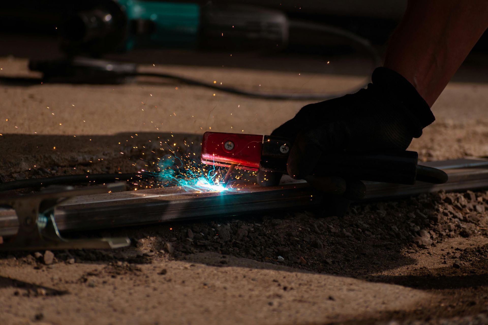 A person is welding a piece of metal on the ground.