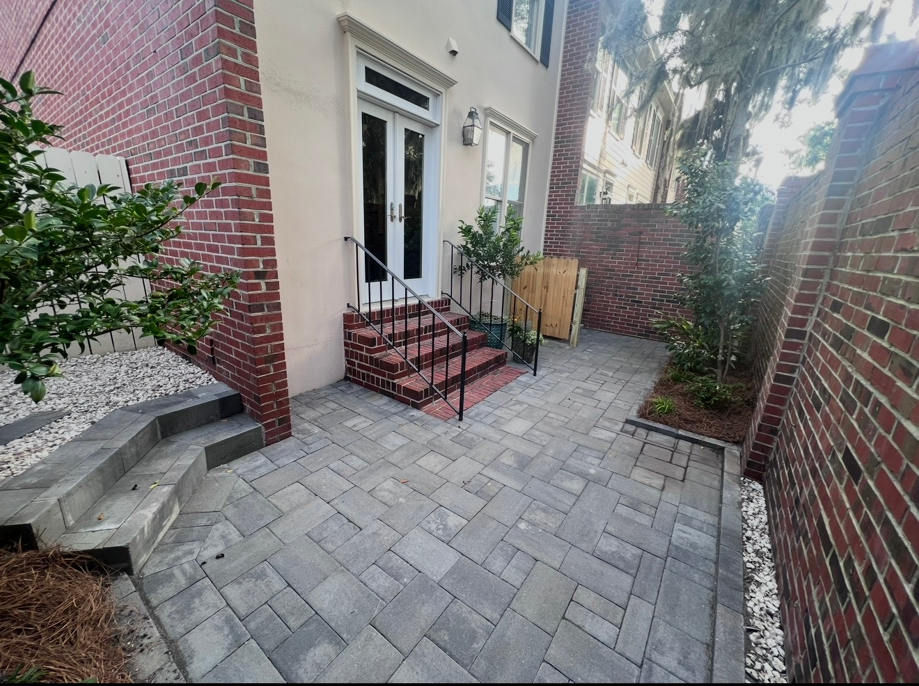 A courtyard with grey stone pavers, brick walls, and steps leading to white double doors on a house.