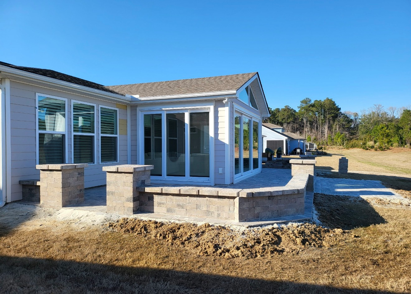 A light-colored house with a sunroom and a new stone patio featuring decorative columns and a built-in curved wall.