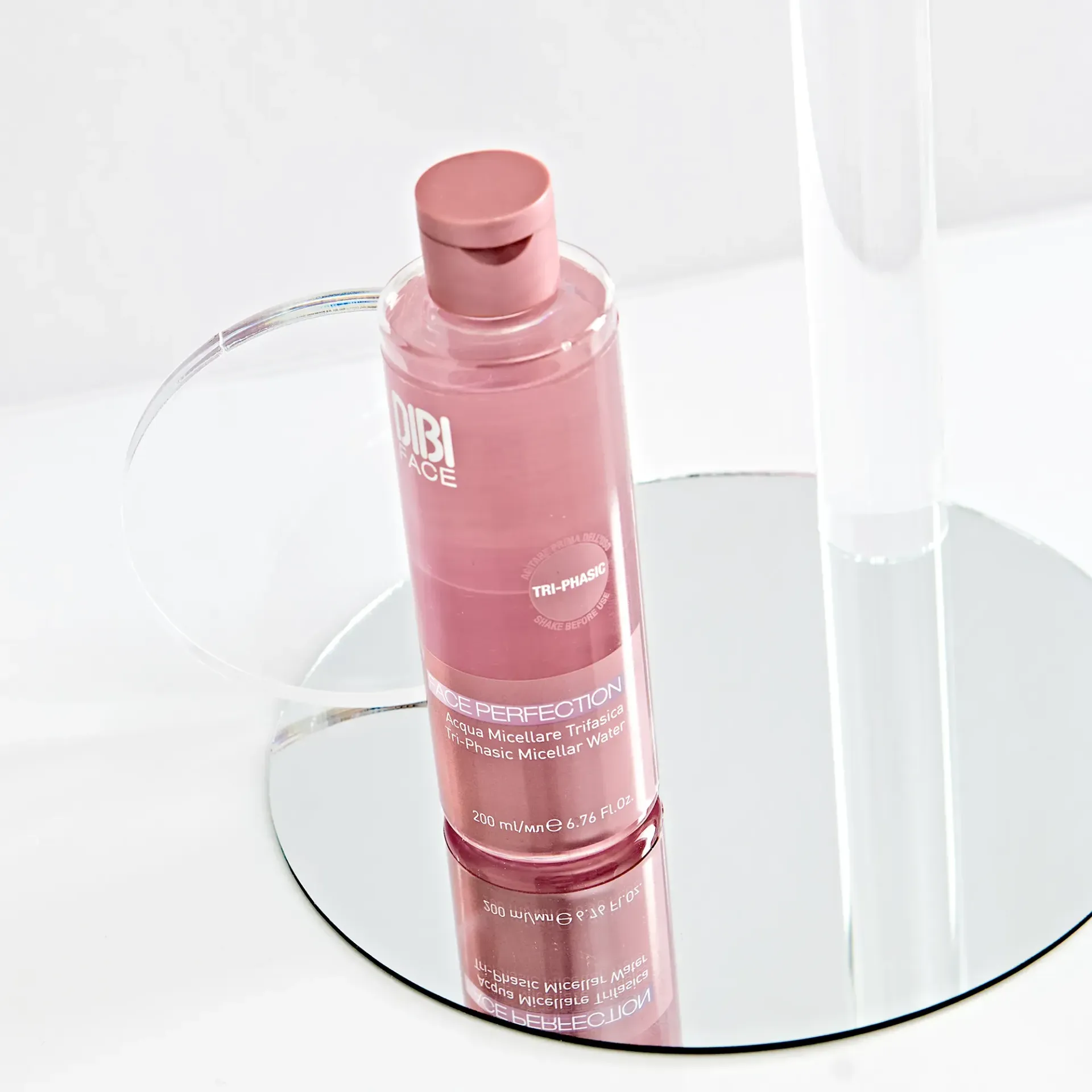 Flacone rosa di prodotto per la cura della pelle su una superficie a specchio, con supporti in acrilico trasparente.
