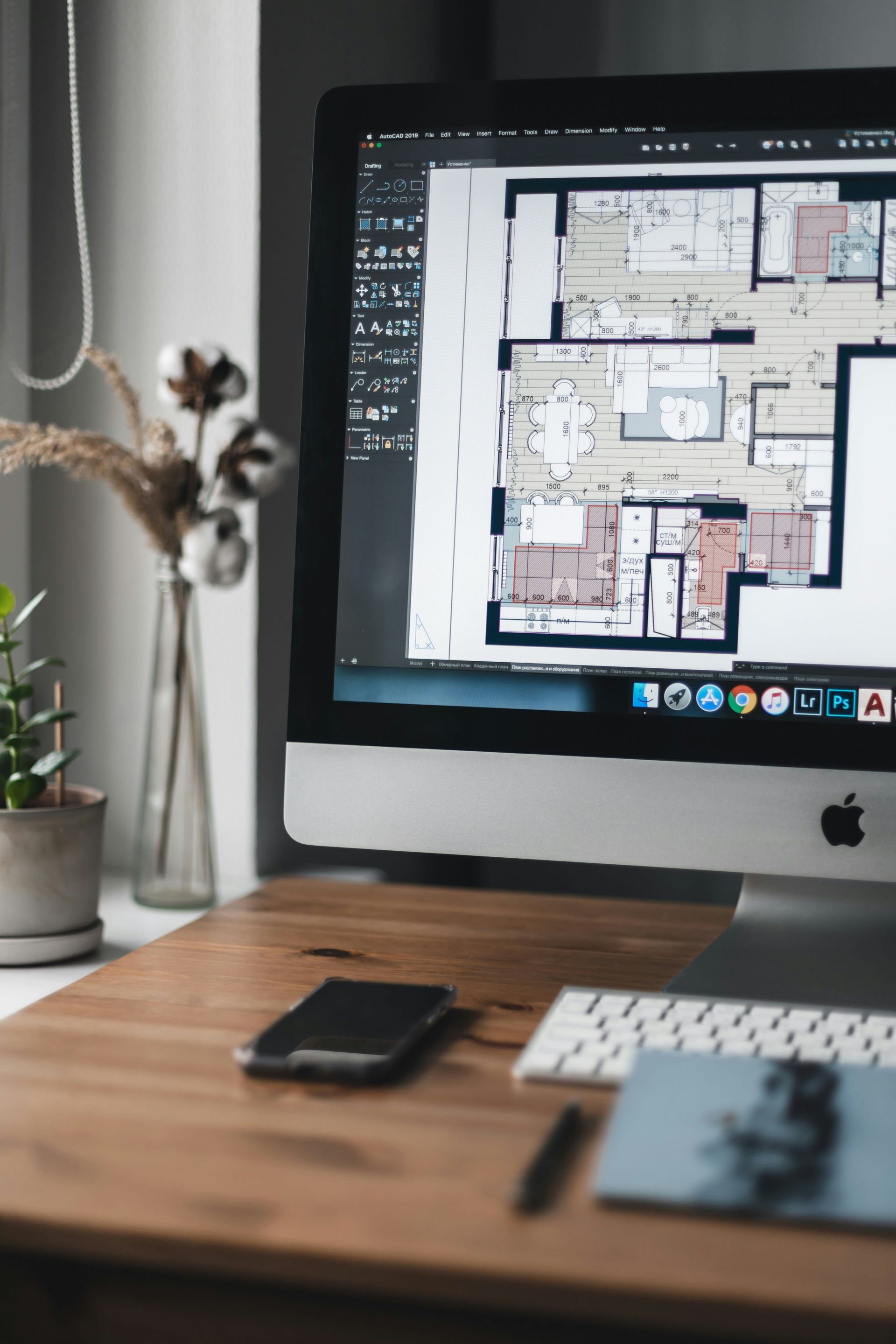 Desktop monitor displaying a floor plan on a desk with a phone, keyboard, and small plant nearby