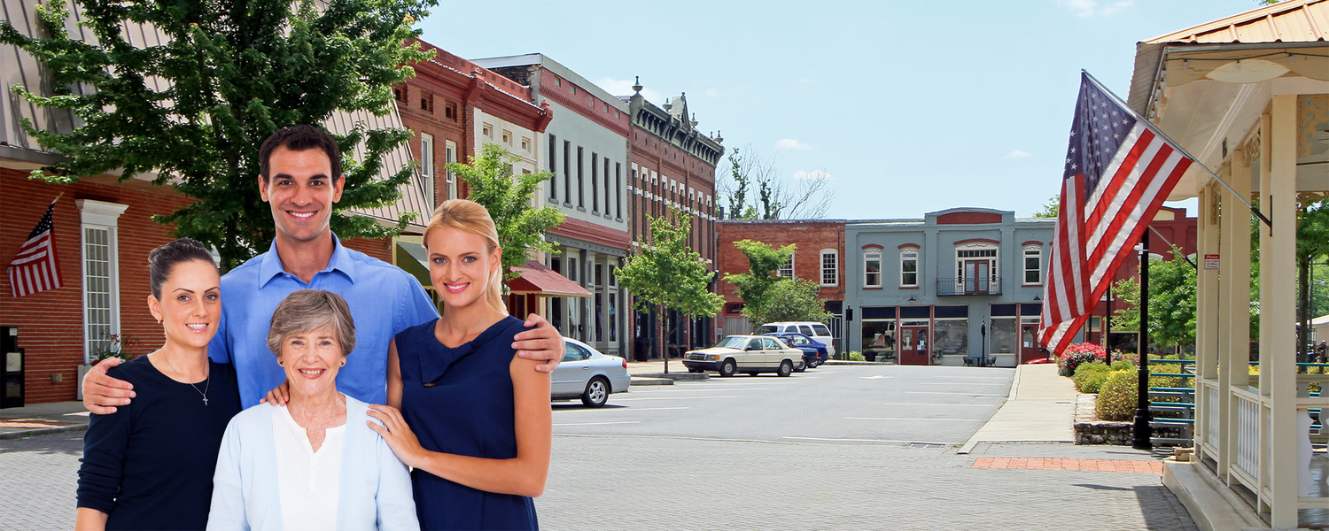 Four people posing on a small-town street with brick buildings and American flags in the background