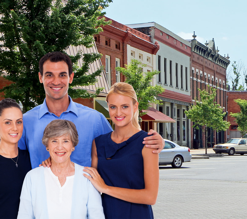 Four smiling people stand on a sunny downtown street in front of brick storefronts.
