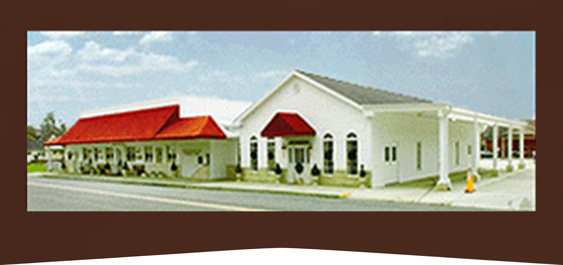 White building with red awnings and roof in a parking lot under a blue sky