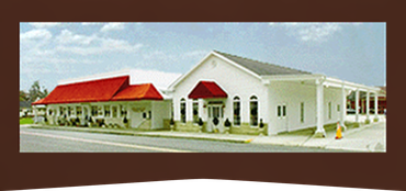White building with red awnings and roof in a parking lot under a blue sky