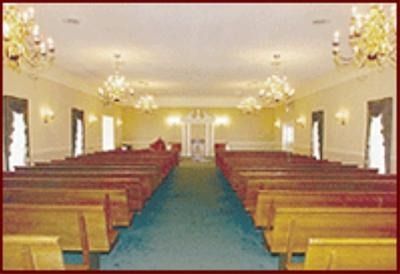Empty church interior with wooden pews, blue carpet, and chandeliers leading to the front altar