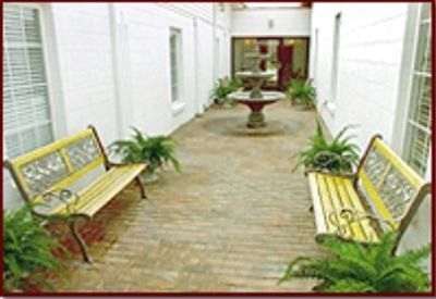 White courtyard with yellow benches, potted plants, and a central fountain on a brick path