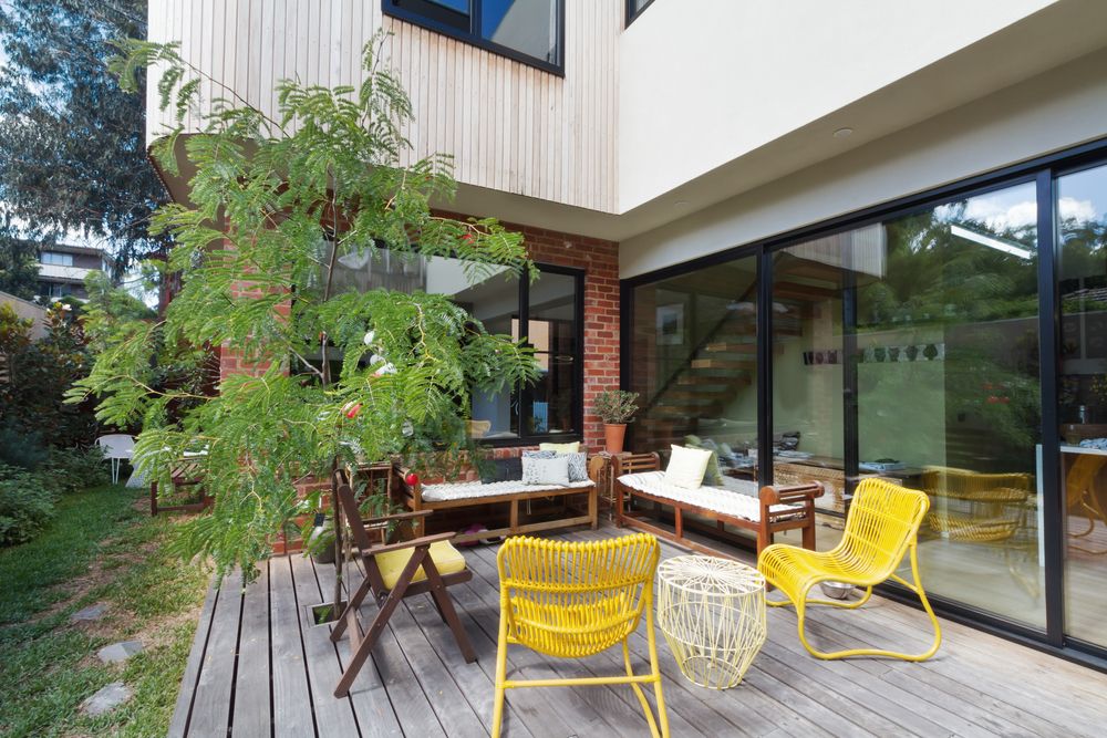 A wooden deck with yellow chairs and a table in front of a house.