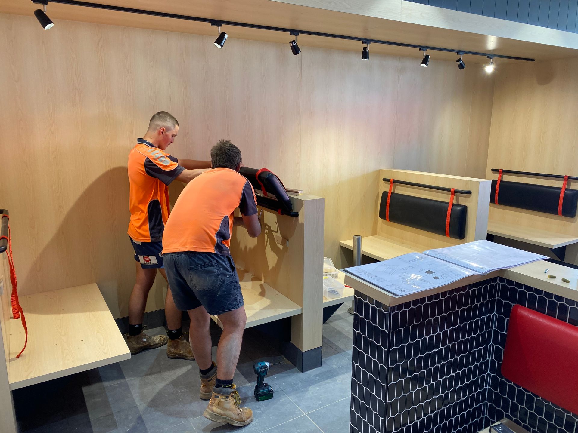 Two construction workers installing booth seating in a restaurant. One is using a drill.