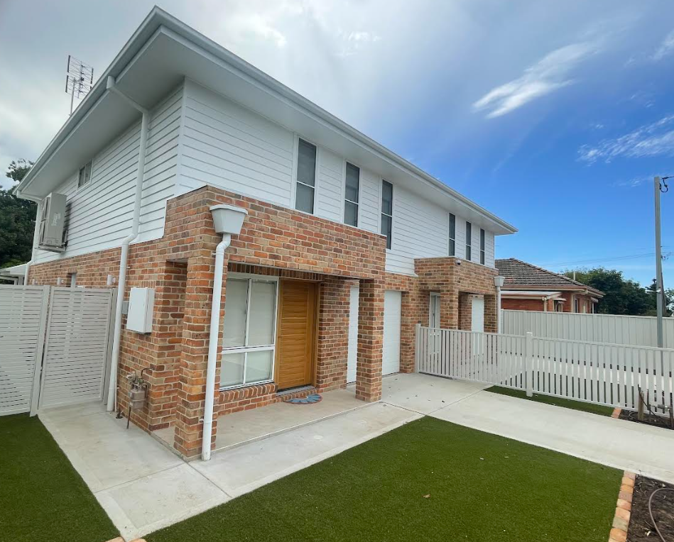 Two-story townhouses with white siding and brick accents. A paved driveway and fenced yard are in front.
