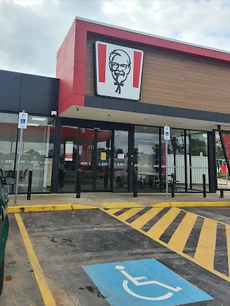 KFC restaurant exterior with the Colonel Sanders logo, glass doors, and a blue handicap parking space.