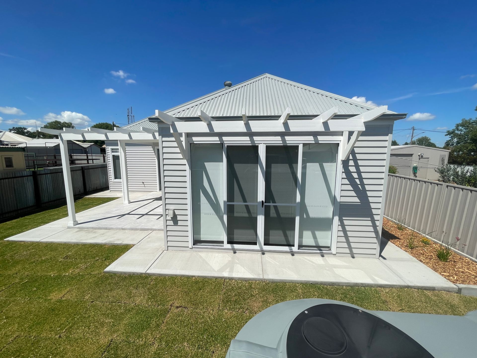A small white house with a pergola and sliding glass doors