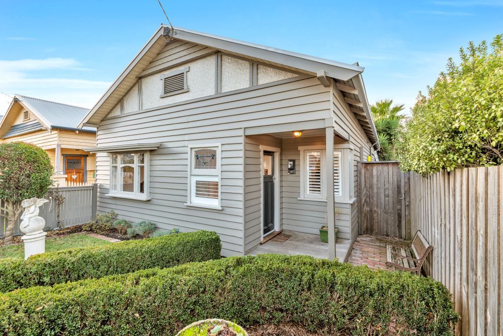 A small house with a porch and a wooden fence in front of it.