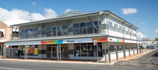 Two-story white building with glass windows, coloured sign, and a street in front.