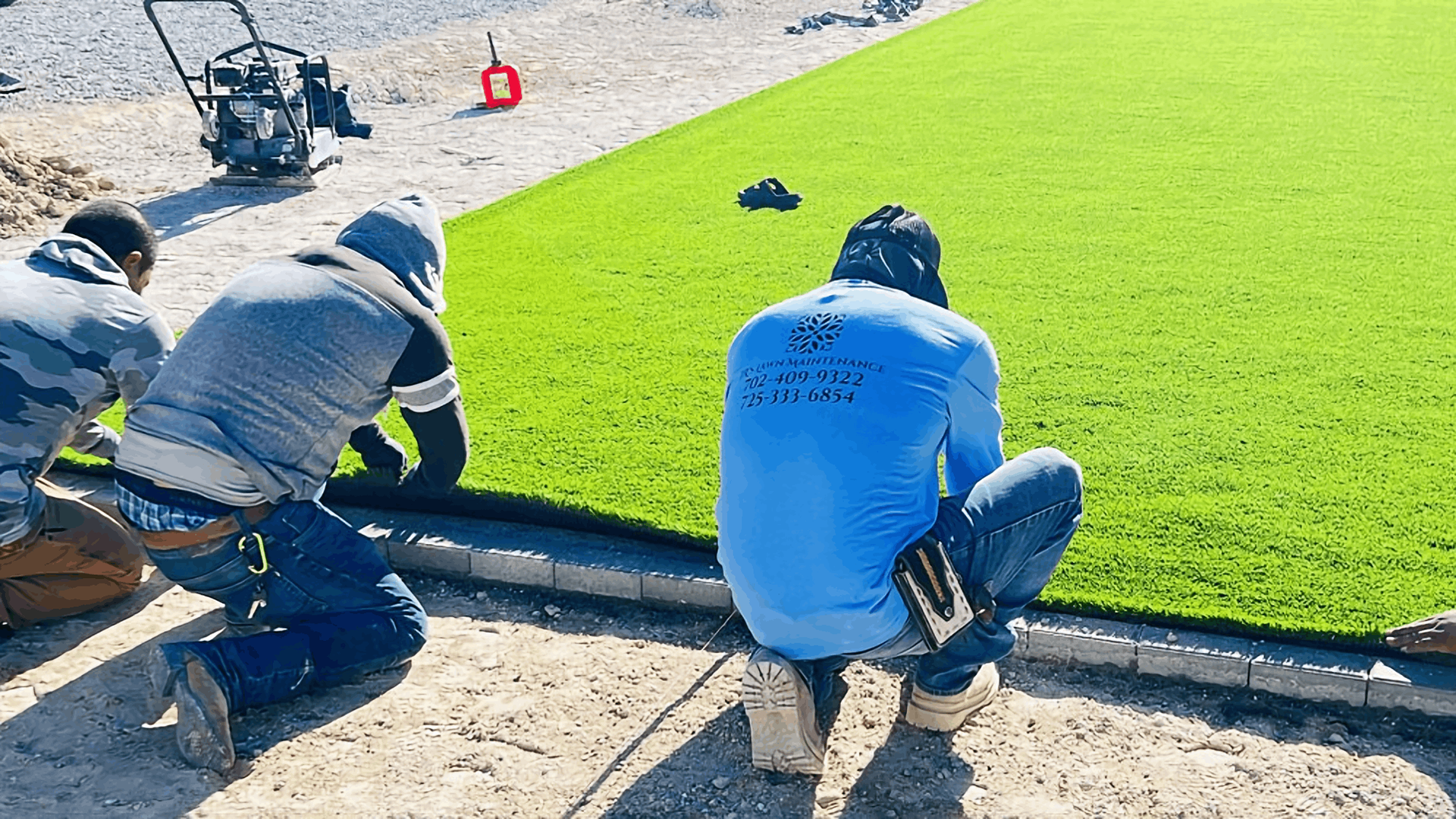 Workers laying bright green sod along a curb on a sunny day