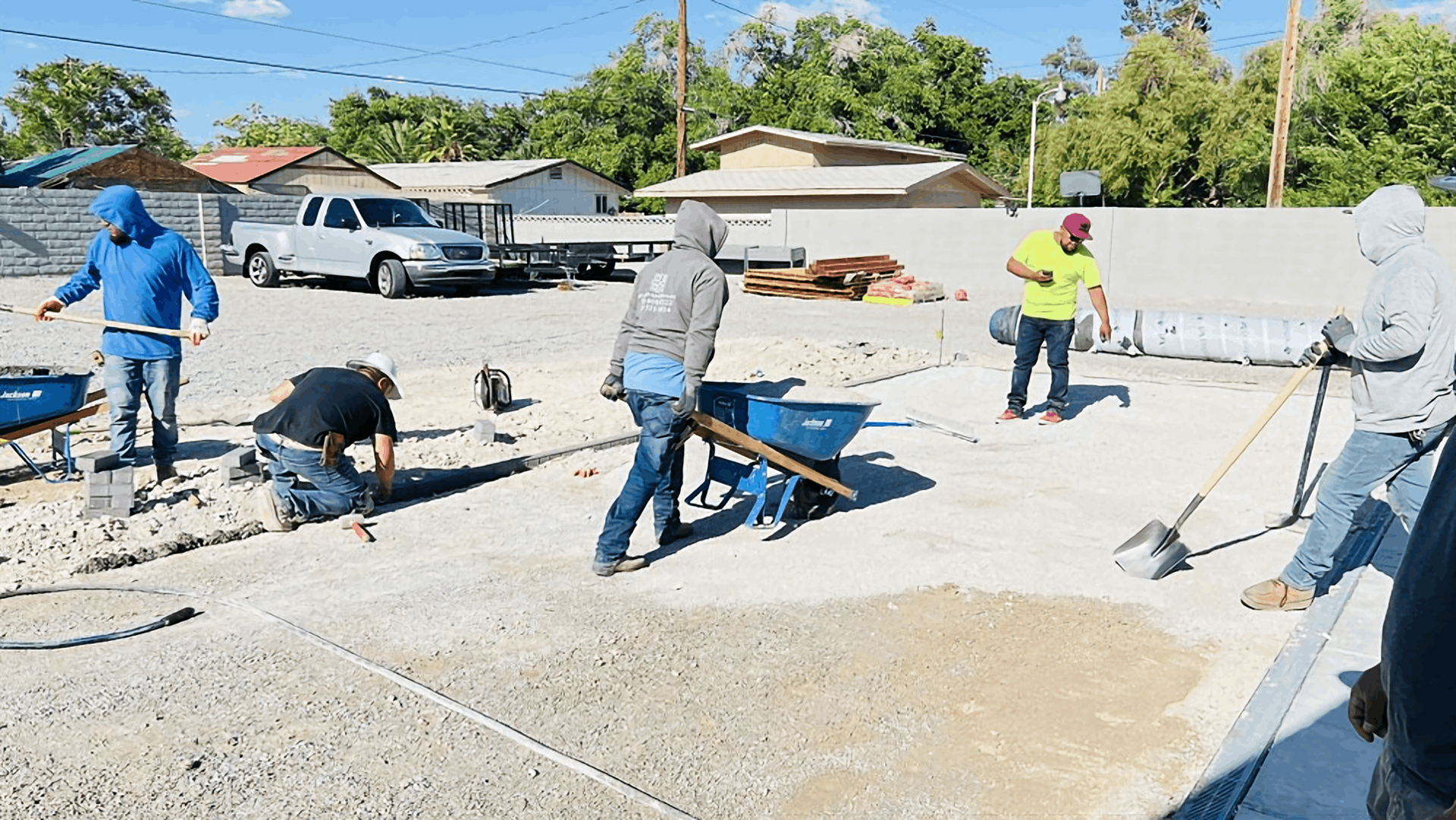 Construction workers pouring and leveling concrete at an outdoor site on a sunny day
