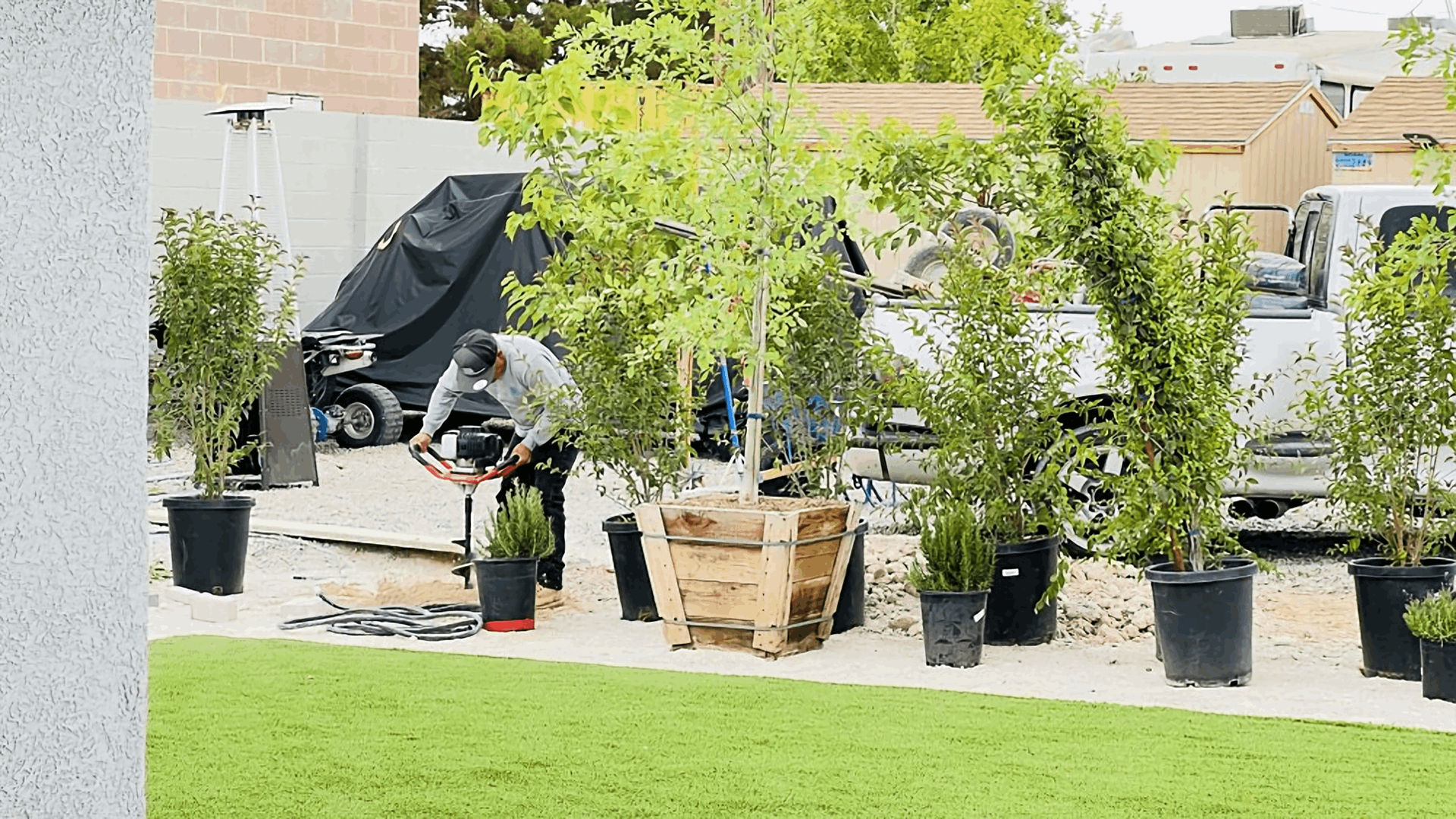 Person gardening among potted plants and a wooden planter in a sunny backyard with a green lawn