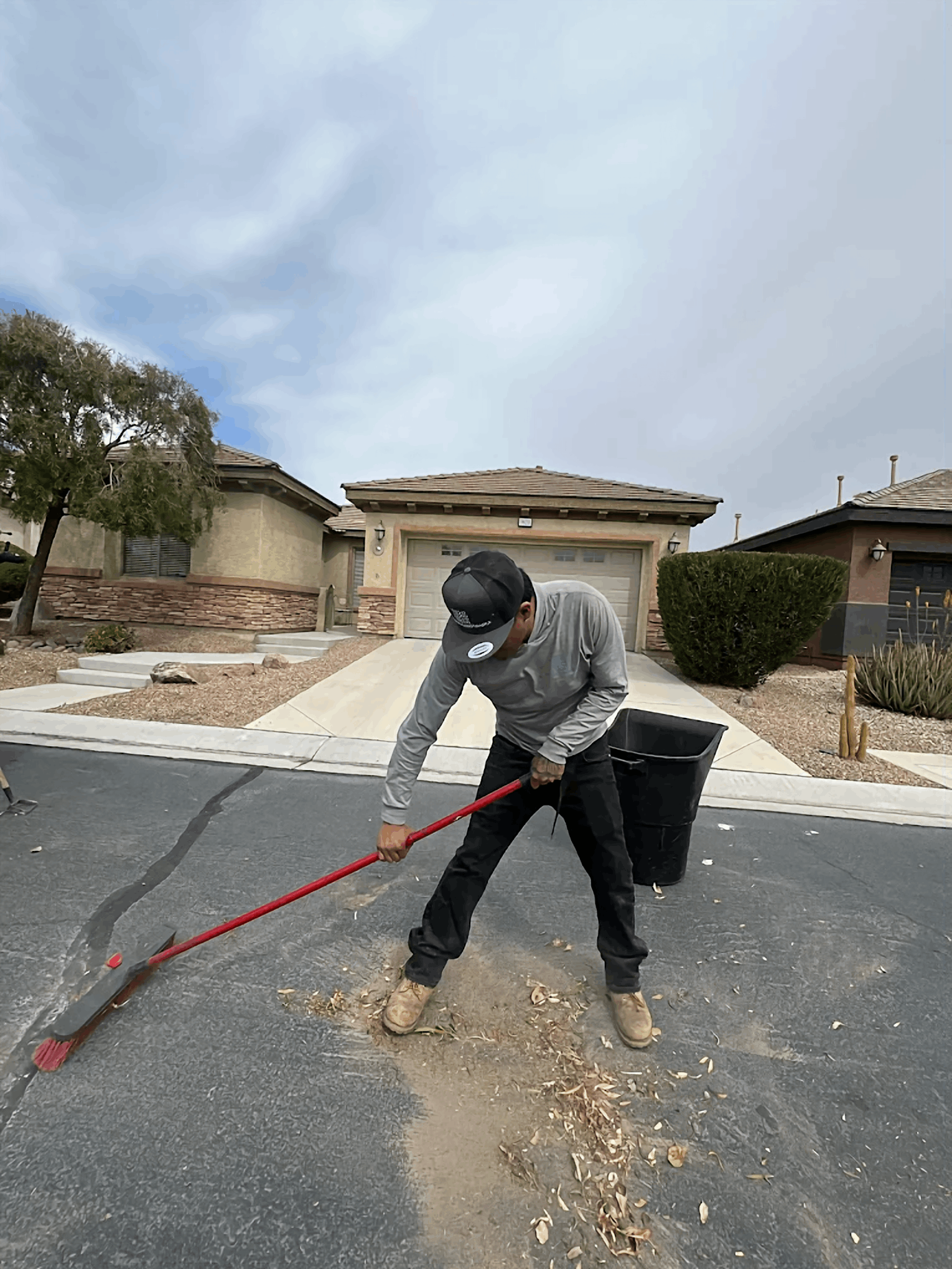 Person sweeping debris from a street with a red broom in front of a house.
