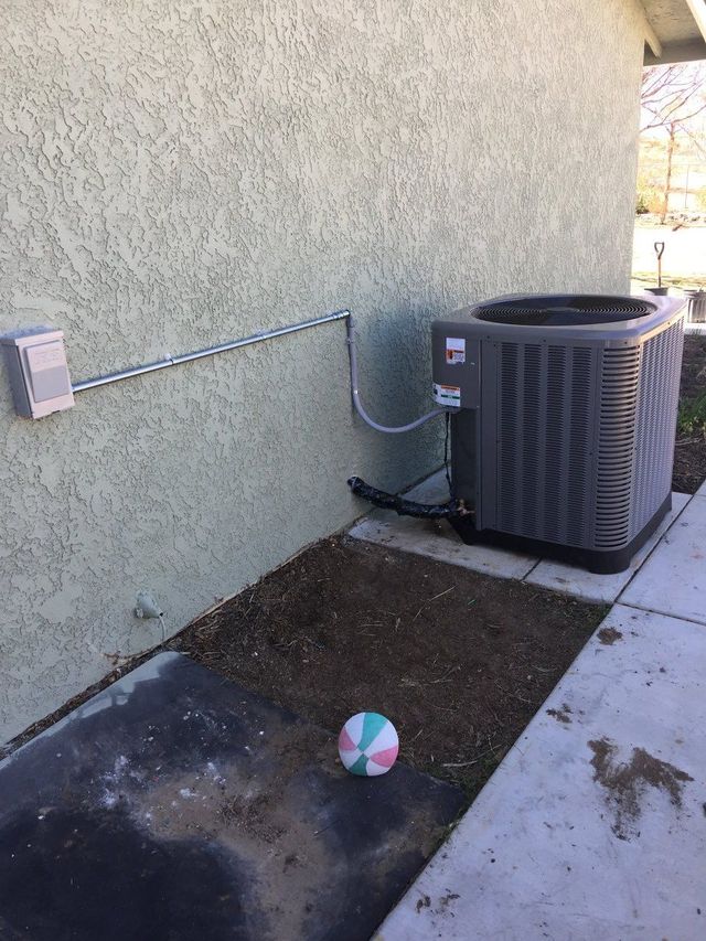 Air conditioning unit next to a building on a concrete slab, with a multi-colored ball in front.